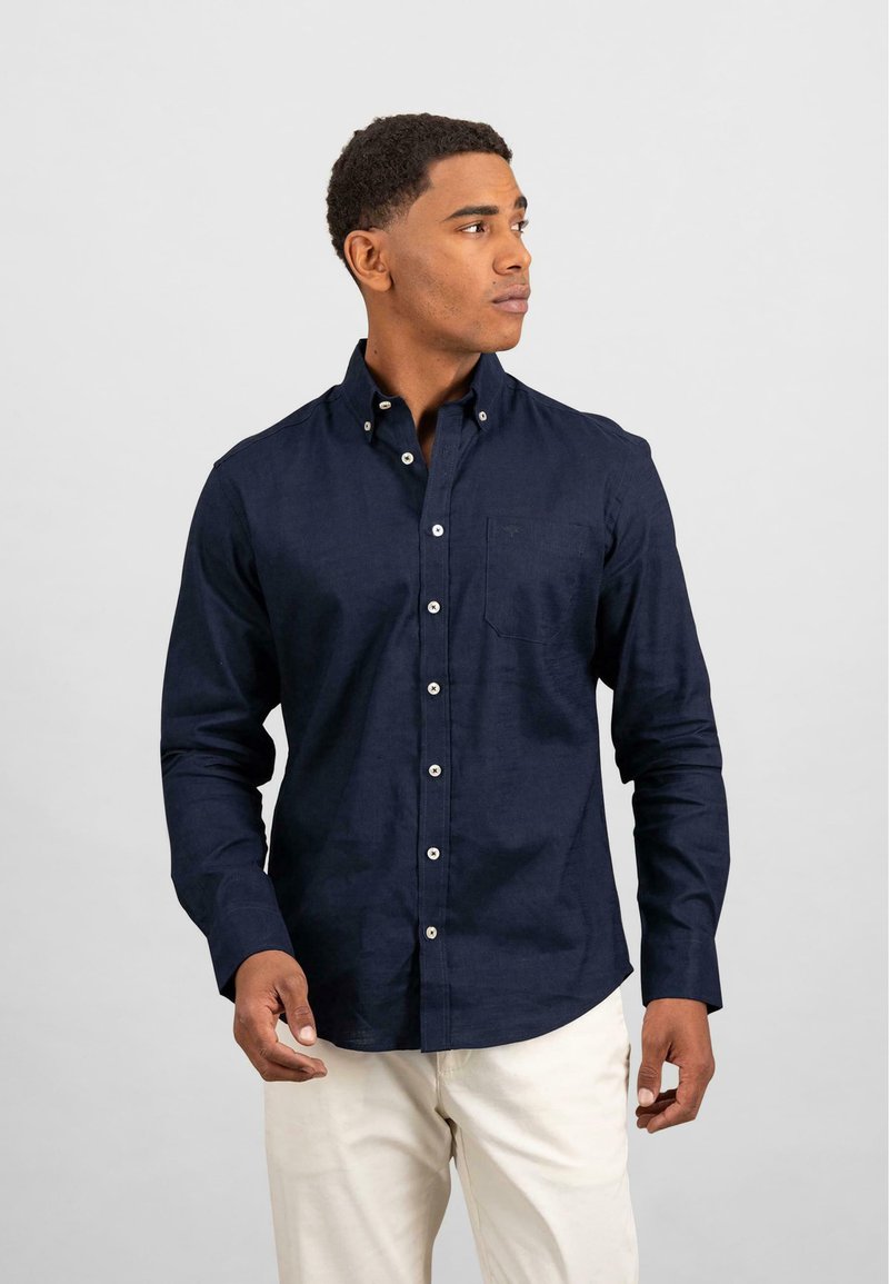 Marineblå skjorte med knapper og lange ermer, liten brystlomme og hvite knapper. Stoffet ser glatt og lett ut.