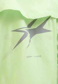 Šviesiai žalia striukė su blizgiu paviršiumi, ant kurios yra didelis pilkas žvaigždės logotipas ir tekstas „CORE—ME.ZERO“ apačioje. Textūruotas audinys.