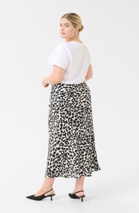 Camiseta blanca de manga corta combinada con una falda de longitud media con un estampado de leopardo en negro y beige, complementada con unos tacones negros tipo slingback.