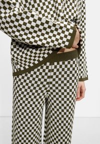 Ensemble en tricot assorti en vert olive et motif à carreaux blancs. Comprend des manches longues et une taille élastique, mettant en valeur une finition texturée.