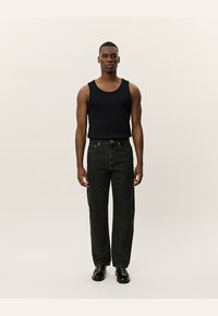 Black tank top, dark denim jeans, standing figure. Jeans feature straight cut, front pockets, and contrasting stitching. Black shoes.