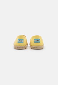 Geel canvas espadrilles met een jute zool. Voorzien van blauwe TOMS-labels aan de achterkant, een ronde vorm en een ademend ontwerp.