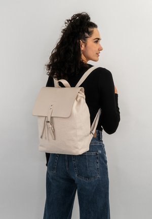 Light beige canvas backpack with a flap closure, adjustable straps, and a minimalistic design. Features a textured fabric and practical hardware.