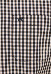 Schwarz-weiße und beige karierte Hemdtasche mit einem kleinen bestickten schwarzen Pferdelogo in der oberen linken Ecke.