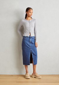 Top grigio a maniche lunghe con coste e chiusura a bottoni, abbinato a una gonna midi in denim blu con spacco frontale e zoccoli beige a piattaforma.