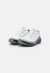 White athletic shoes with a textured fabric upper, featuring grey accents and a curved, cushioned sole designed for comfort and support.