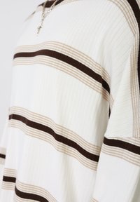 Λευκό και εκρού ριμπ πουλόβερ με οριζόντιες καφέ και μπεζ ρίγες. Διαθέτει άνετη εφαρμογή και στρογγυλή λαιμόκοψη.