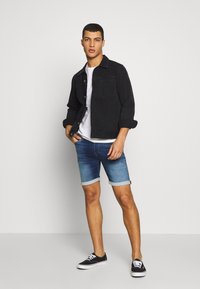 Svart denimjacka, vit T-shirt och blå denimshorts med uppvikta fållar. Svarta sneakers fulländar outfiten. Enkelt, avslappnat stil.