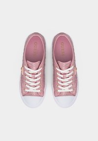 Paire de baskets Guess en tissu tissé rose avec lacets blancs et embouts, œillets dorés, et logo sur les semelles intérieures et les étiquettes latérales.