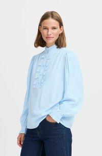 Hellblaues langärmliges Bluse mit hohem Kragen, gerüschter Vorderblende und gerafften Manschetten. Aus weichem Stoff mit glatter Textur gefertigt.