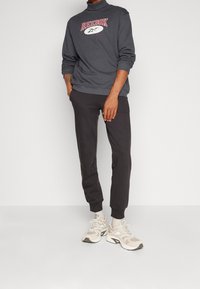 Šedá mikina se znakem 'Reebok Classic', černé zúžené kalhoty a béžové tenisky s bílými detaily a texturovanou podešví.