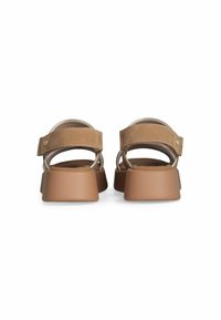 Brune ruskindssandaler har en bred ankelrem og en kraftig, solid tan platformsål. Synlige hardware-dekorationer tilføjer detaljer.