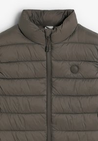 Giacca a vento in grigio scuro, con un alto collo e texture trapuntata. Presenta una zip frontale e un logo circolare sul petto sinistro.