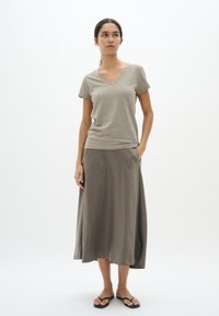 Lichtgrijze V-hals t-shirt gecombineerd met een knielange, vloeiende bruine rok en zwarte slippers. Eenvoudig ontwerp, soepele textuur, casual uitstraling.