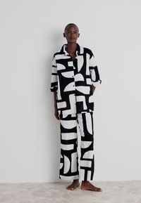 Conjunto de pijama de estampado en blanco y negro hecho de tela suave. Presenta una camisa con botones y mangas recogidas, y pantalones sueltos.