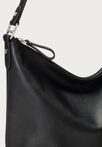 Μαύρη δερμάτινη τσάντα χειρός με λεία υφή, καμπύλο σχέδιο και ασημένιες λεπτομέρειες. Διαθέτει κλείσιμο με φερμουάρ και ρυθμιζόμενο λουράκι.