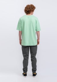 T-shirt oversize verde menta con maniche corte, abbinato a pantaloni jogger grigio scuro e scarpe da ginnastica nere con dettagli gialli.
