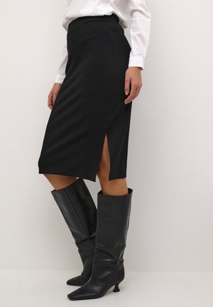 Black knee-length skirt with a fitted silhouette, featuring a side slit. Paired with tall black leather boots, showcasing a pointed toe design.