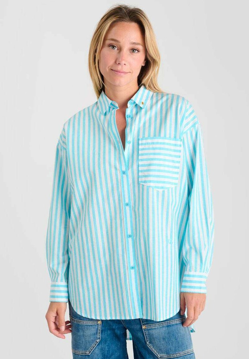 Femme portant une chemise boutonnée à manches longues et amples avec des rayures verticales turquoise et blanches, associée à un pantalon en denim bleu avec des poches avant.