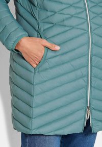 Gevoerde teal buitenkleding met een ritsluiting en zijzakken, ontworpen met een slanke, gestroomlijnde vorm en een gladde textuur.