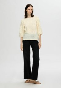 Texturerad krämfärgad tröja med en gradvis färgövergång, kombinerad med högmidjade svarta jeans och beige ballerinas. Har 3/4 ärmar.