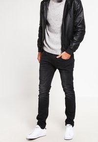 Zwarte jeans, grijze geribbelde trui en een zwarte leren jas; witte sneakers maken de outfit compleet; casual pasvorm met een gestroomlijnde silhouet.