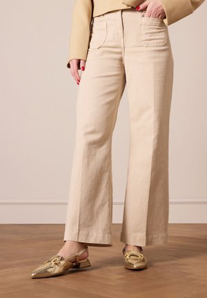 Beige wijdvallende broek in katoenmix, met twee achterzakken en een subtiele textuur, gecombineerd met metallic gouden slingback schoenen.