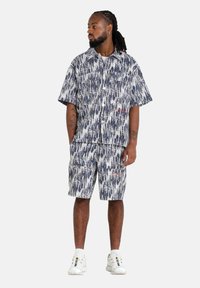 Korte mouwen shirt en short set in marineblauw met een wit abstract patroon, met een kraag, knoopsluiting aan de voorkant en zakken op de shorts.