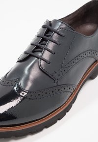 Scarpa elegante in pelle blu con finitura lucida, design a punta di diamante, dettagli perforati, chiusura con lacci e suola in gomma resistente.