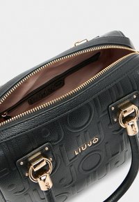 Sac à main en cuir noir texturé avec quincaillerie dorée, motif logo embossé et intérieur rose clair. Dispose de poignées supérieures doubles et d'une fermeture zippée.