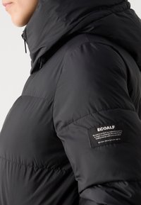 Black puffer jacket with a high collar, made from smooth, lightweight material. Features a logo patch on the sleeve.