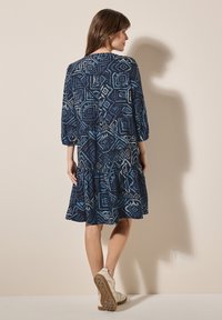 Blå mönstrad klänning med diamant- och geometriska mönster, trekvartslånga ärmar och utsvängd kjol; tillsammans med ljusa sneakers.