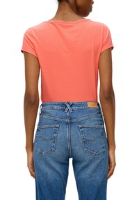 Koraalkleurig katoen t-shirt met korte mouwen, gecombineerd met high-waisted blauwe denim jeans met een klassiek ontwerp met vijf zakken en gestikte accenten.