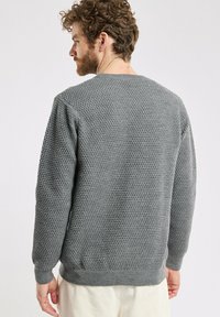 Pull en maille gris avec un motif texturé, col rond et poignets et ourlet côtelés. Le matériau semble doux et chaud.