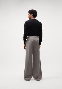 Pull noir à col rond associé à un pantalon gris à jambes larges. Le pantalon a une texture lisse et des poches arrière visibles.