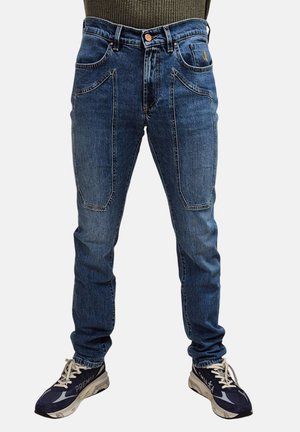 Jeans in denim blu con una vestibilità slim, dotati di due tasche frontali e dettagli di cucitura sottili. Abbinati a scarpe da ginnastica scure.