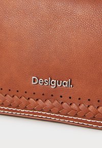 Portafoglio in pelle marrone con texture intrecciata nella parte inferiore, dettagli in cucitura bianca e logo "Desigual" in argento.