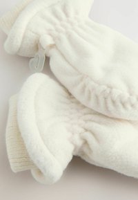 Soft white fleece mittens with ribbed cuffs, connected by a plastic clip, laid on a flat light surface.