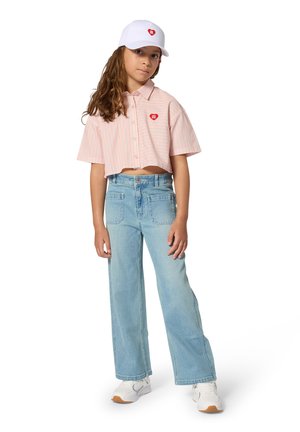 Cropped pink and white striped shirt with a heart logo, paired with light blue wide-leg jeans and white sneakers. White cap completes the look.
