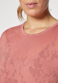 Pink short-sleeve T-shirt with a round neckline, made of a smooth fabric featuring a subtle abstract pattern across the surface.