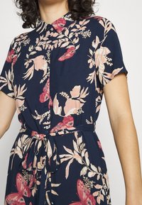 Abito camicia floreale in blu navy con motivi botanici rosa e bianchi, maniche corte, colletto e dettaglio in vita legato per un look aderente.