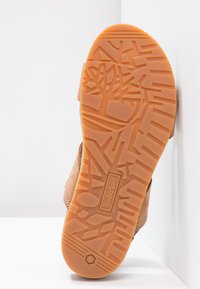 Brun lær såle med et teksturert mønster og preget Timberland-logo. Yttersålen er oransje med geometriske former for grep.