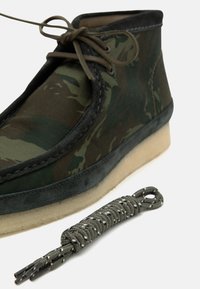 Gröna kamouflage-ankelboots med övre i mjukt mockamaterial och ljust gummisulor. Inkluderar matchande mönstrade skosnören bredvid skon.