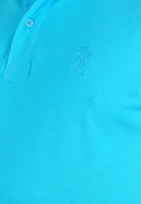 Turkos polo t-shirt i strukturerad tyg, med en treknappslåning och en präglad U.S. Polo Assn. logotyp på bröstet.