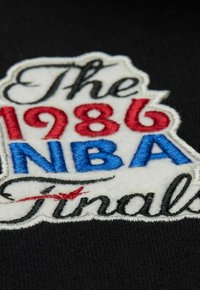 Tejido negro que presenta un parche bordado con "Las Finales de la NBA de 1986" en texto rojo, azul y negro, contorneado en hilo blanco.