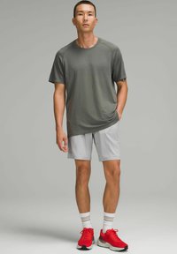 Grå træningsshirt med korte ærmer, parret med lysegrå shorts. Outfittet er kompletteret med røde løbesko og hvide sokker.