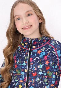 Farverig zip-up jakke med et marineblåt stof og akvatiske mønstre, herunder blæksprutter, fisk og bobler, med en blød tekstur og hætte.