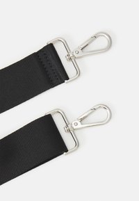 Sangle en nylon noir équipée de deux crochets métalliques à chaque extrémité. La sangle présente une finition texturée avec des coutures renforcées.