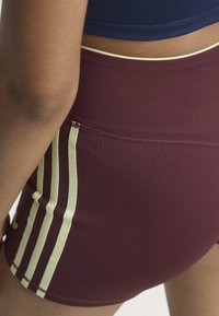 Close-up of a person wearing burgundy athletic shorts with three light-colored vertical stripes on the side and a navy blue top.