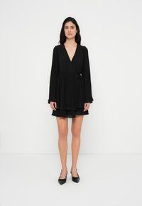 Μαύρο φόρεμα τύπου wrap με μακριά μανίκια, υφασμάτινη υφή και στρωματοποιημένη φούστα. Διαθέτει βαθύ V-neck και ζώνη στη μέση για ρυθμιζόμενη εφαρμογή.